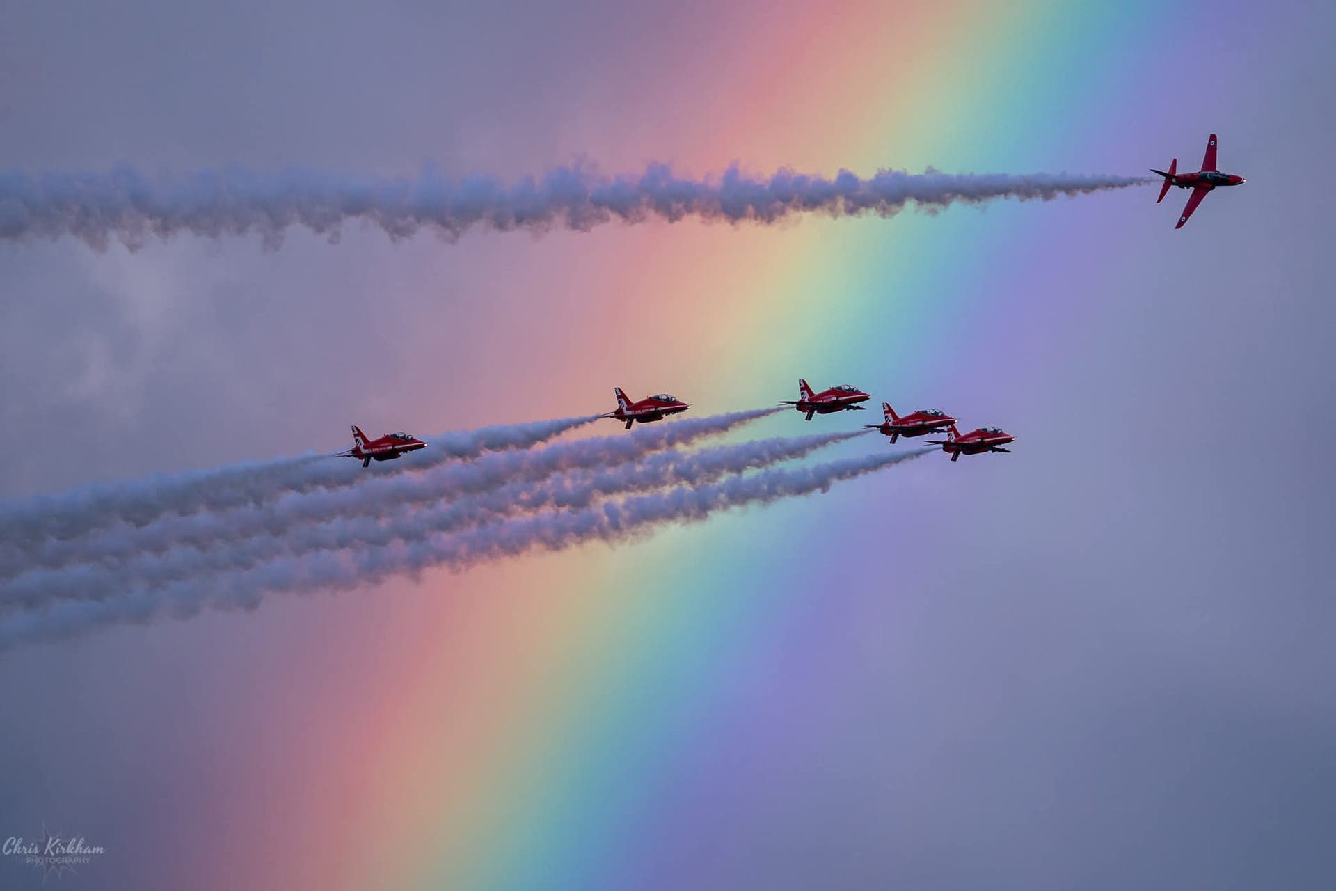 The Red Arrows flying in formation trailing smoke in front of a rainbow