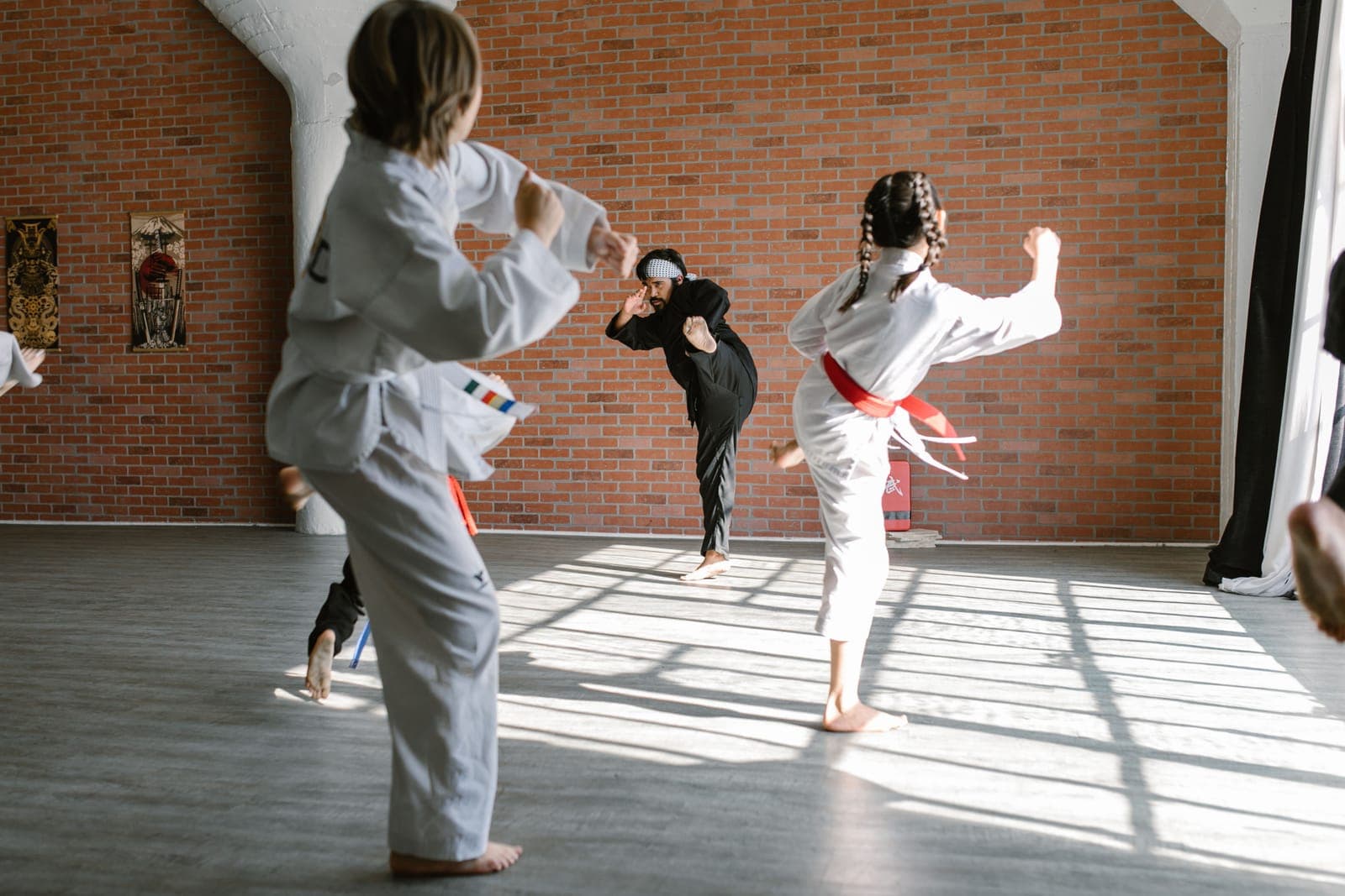 Children in karate uniforms practising kicks with an instructor in a sunlit studio