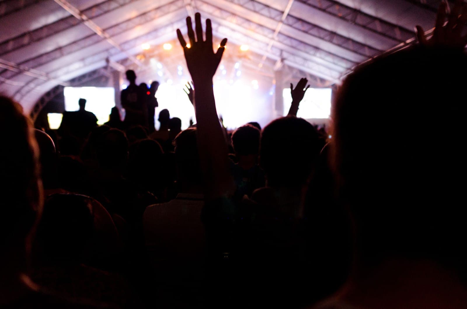 A crowd with hands raised in front of a brightly lit stage inside a large festival tent