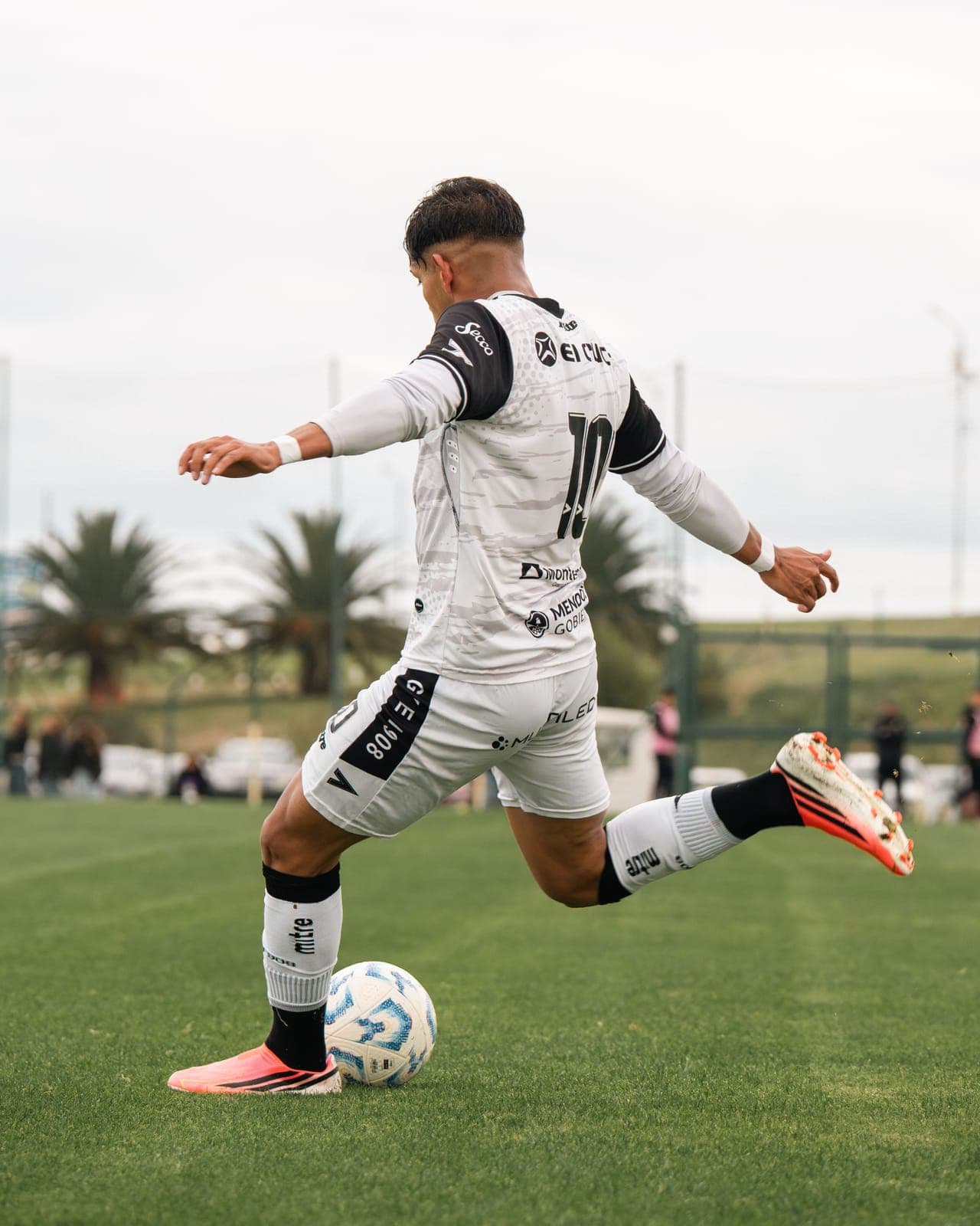 A footballer in a white kit about to strike the ball on a grass pitch